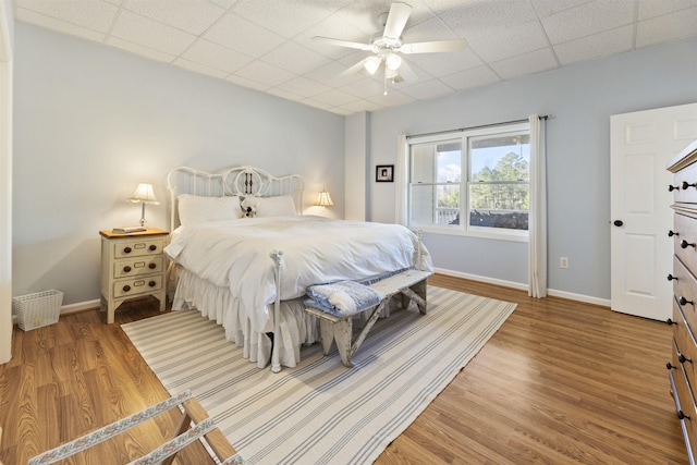 bedroom with a ceiling fan, a drop ceiling, baseboards, and wood finished floors