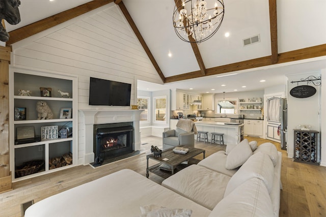 living room featuring light wood-style floors, a fireplace with flush hearth, visible vents, and beamed ceiling