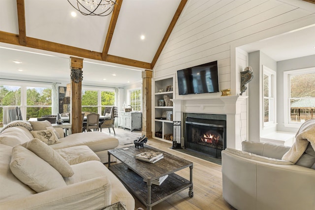 living area with high vaulted ceiling, built in shelves, a fireplace with flush hearth, light wood-type flooring, and beam ceiling