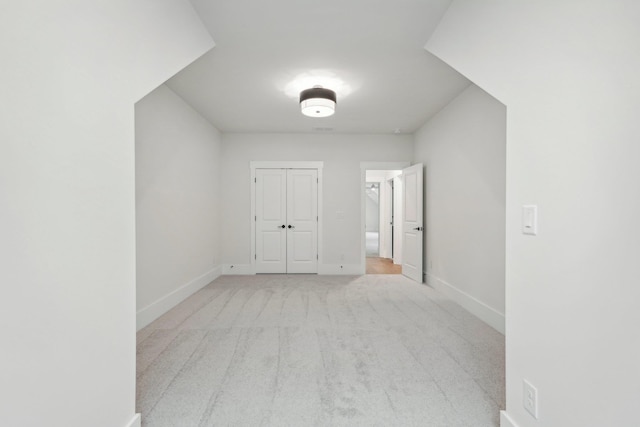 interior space featuring a closet, baseboards, and light colored carpet