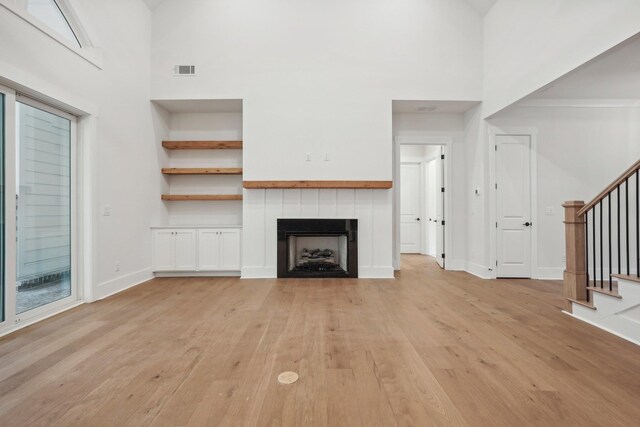 unfurnished living room featuring visible vents, light wood-style flooring, stairway, a fireplace, and baseboards