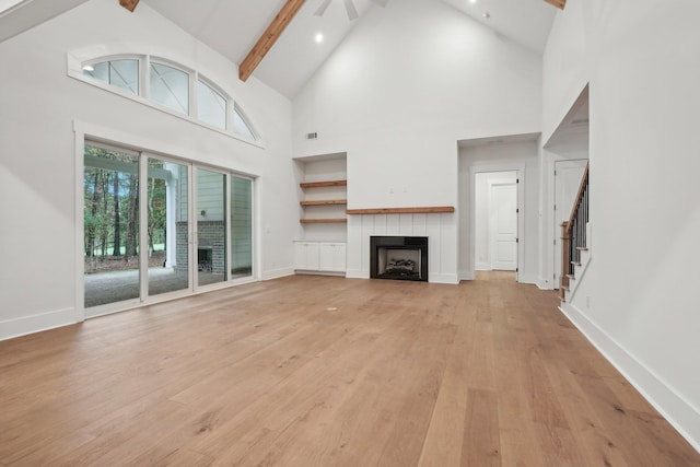 unfurnished living room with light wood finished floors, beamed ceiling, a tile fireplace, and baseboards