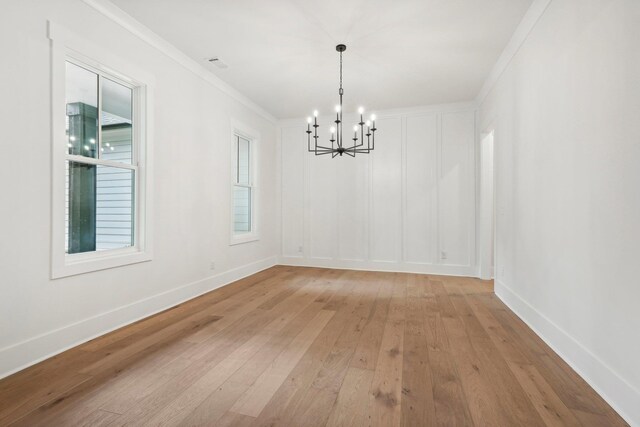 unfurnished room with baseboards, a chandelier, ornamental molding, light wood-style flooring, and a decorative wall