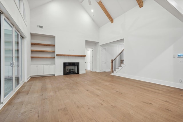 unfurnished living room featuring visible vents, beamed ceiling, stairs, light wood-style flooring, and a fireplace