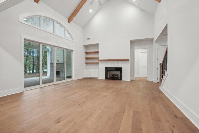 unfurnished living room with stairway, baseboards, light wood finished floors, a fireplace, and beamed ceiling