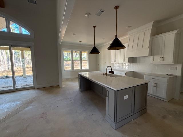 kitchen with visible vents, custom range hood, decorative backsplash, white cabinetry, and a sink