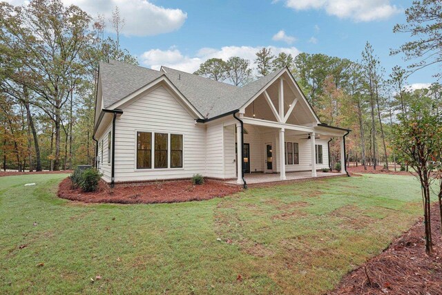 view of front of house with a shingled roof, ceiling fan, a front lawn, and a patio area