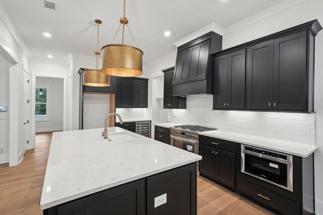 kitchen with premium range hood, visible vents, a sink, crown molding, and dark cabinets