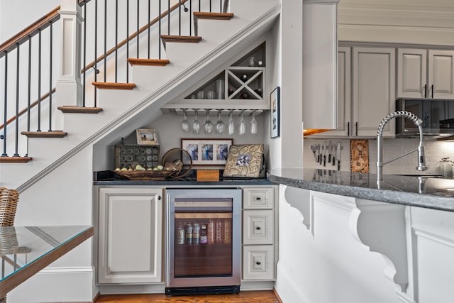 bar featuring gray cabinets, sink, beverage cooler, decorative backsplash, and dark stone counters