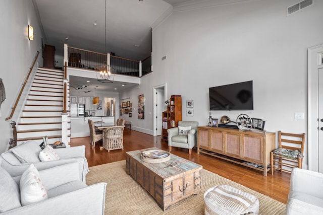 living room with crown molding, a towering ceiling, a chandelier, and light wood-type flooring