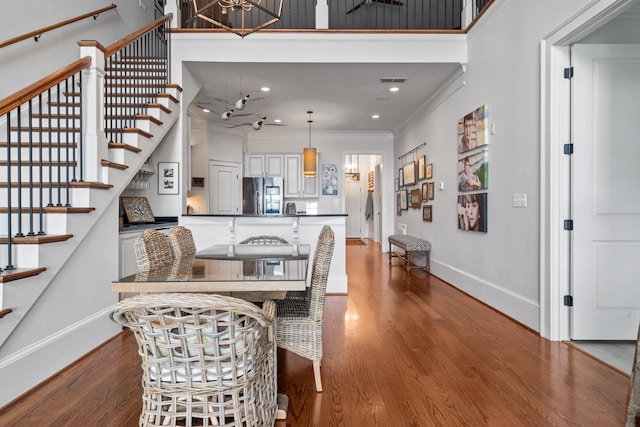 dining room featuring a towering ceiling, wood-type flooring, and ornamental molding