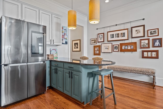 kitchen featuring stainless steel refrigerator, a breakfast bar area, hanging light fixtures, kitchen peninsula, and crown molding