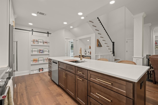 kitchen featuring sink, appliances with stainless steel finishes, hardwood / wood-style floors, an island with sink, and a barn door