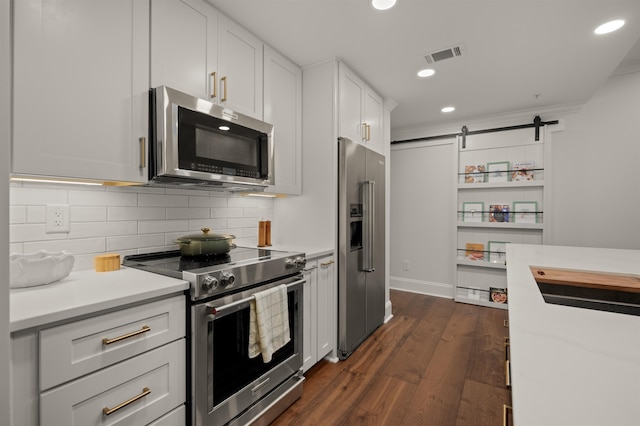 kitchen featuring appliances with stainless steel finishes, dark hardwood / wood-style floors, white cabinetry, backsplash, and a barn door