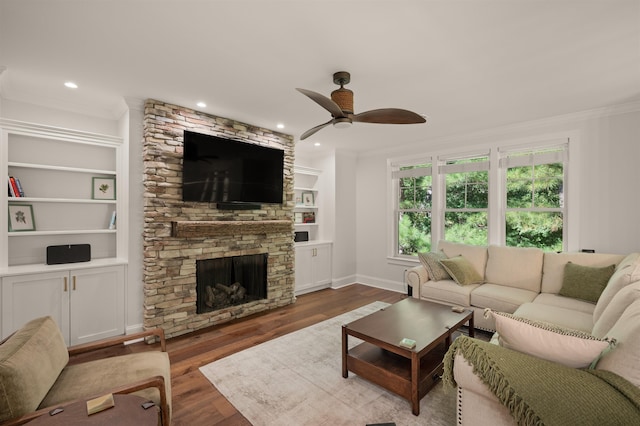 living room with a stone fireplace, crown molding, dark hardwood / wood-style flooring, built in features, and ceiling fan