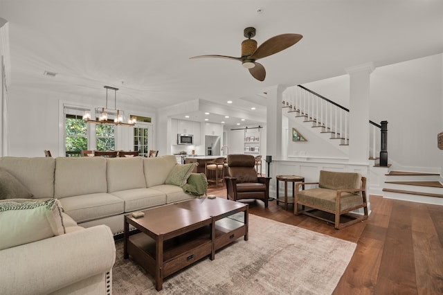 living room featuring crown molding, hardwood / wood-style flooring, ceiling fan with notable chandelier, and ornate columns