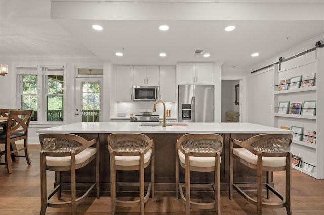 kitchen featuring appliances with stainless steel finishes, a barn door, a large island with sink, and white cabinets