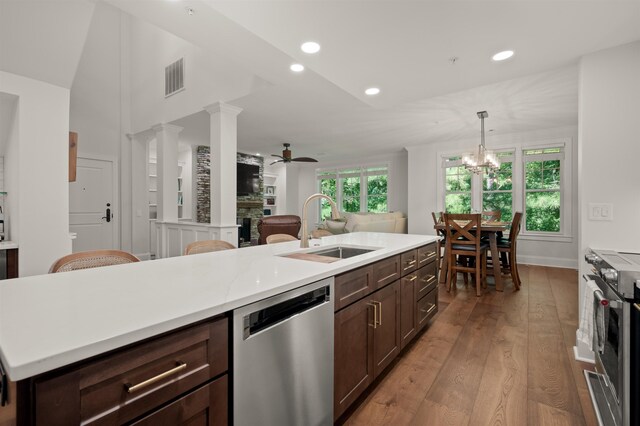 kitchen featuring appliances with stainless steel finishes, a fireplace, an island with sink, sink, and light wood-type flooring