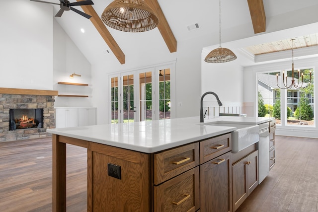 kitchen with sink, a kitchen island with sink, hanging light fixtures, hardwood / wood-style floors, and a fireplace