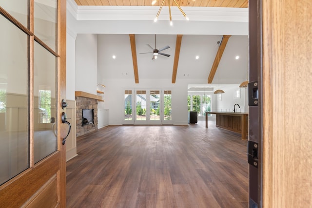 unfurnished living room featuring beam ceiling, dark hardwood / wood-style flooring, a stone fireplace, and high vaulted ceiling