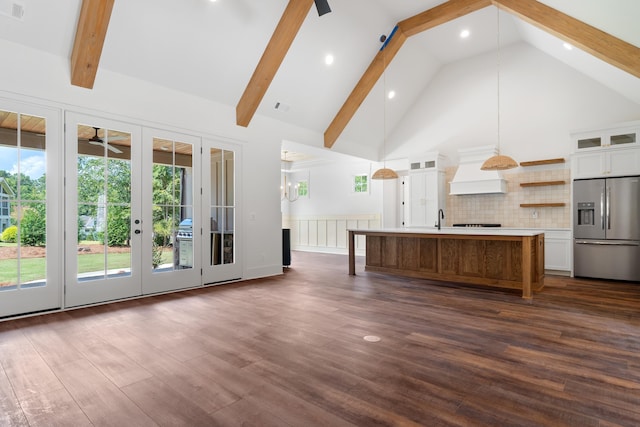 kitchen featuring decorative light fixtures, white cabinetry, an island with sink, stainless steel fridge, and beam ceiling