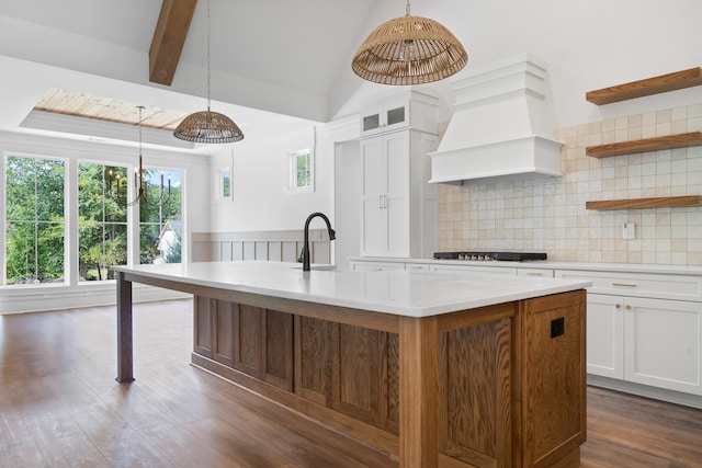 kitchen with white cabinets, hanging light fixtures, black gas stovetop, custom range hood, and a center island with sink