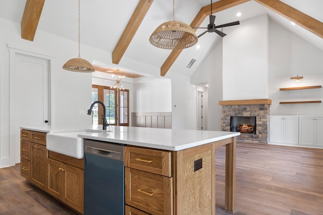 kitchen with a stone fireplace, pendant lighting, dishwasher, an island with sink, and sink