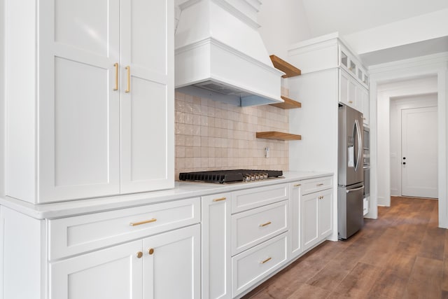 kitchen featuring premium range hood, white cabinetry, appliances with stainless steel finishes, hardwood / wood-style flooring, and decorative backsplash