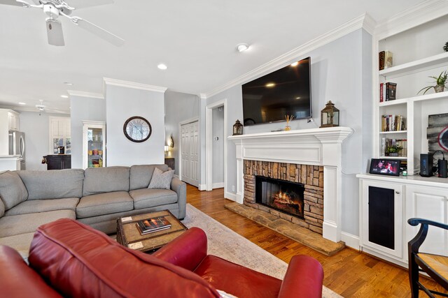 living area with crown molding, ceiling fan, recessed lighting, a warm lit fireplace, and wood finished floors