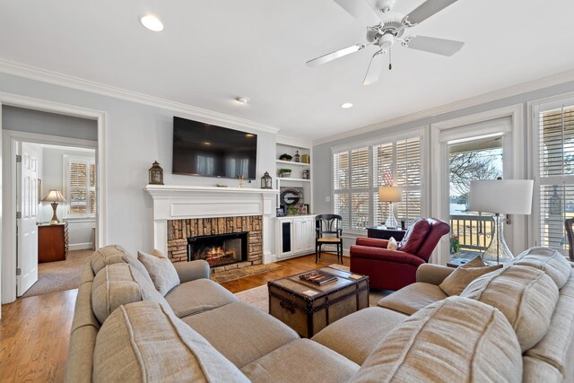 living area with ceiling fan, light wood-style floors, ornamental molding, and a fireplace