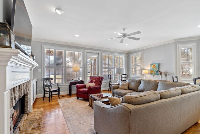 living room featuring a stone fireplace, crown molding, wood finished floors, and a healthy amount of sunlight