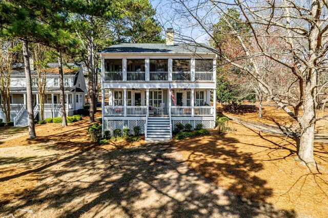 view of front of home with a sunroom, a porch, stairs, a shingled roof, and a chimney