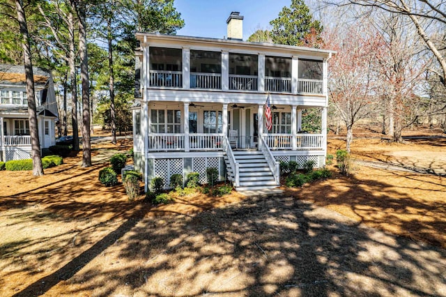 view of front facade with ceiling fan, stairway, a sunroom, and a chimney