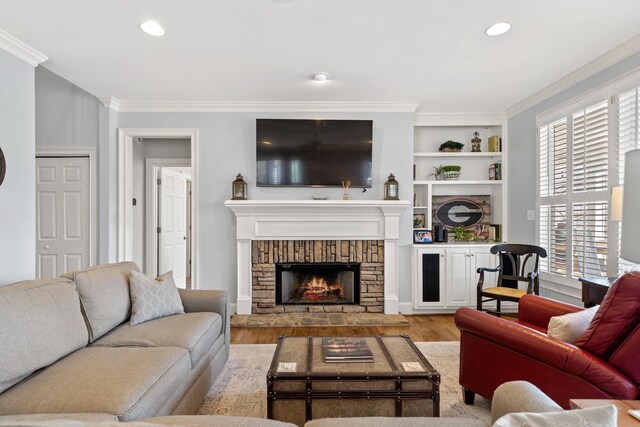 living area with built in shelves, light wood-style flooring, ornamental molding, a warm lit fireplace, and recessed lighting