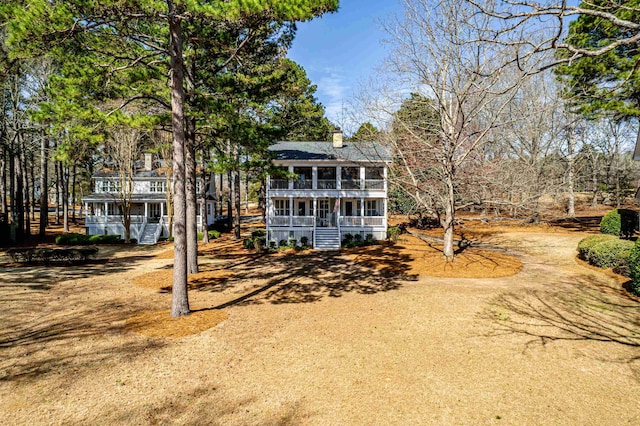 back of house featuring a porch, a balcony, and dirt driveway