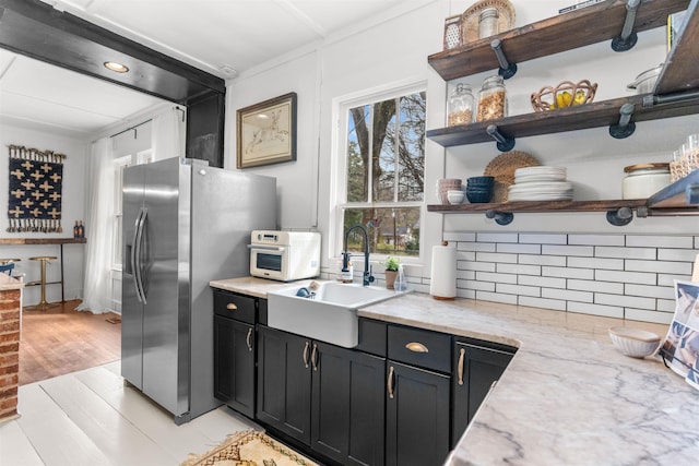 kitchen featuring dark cabinetry, open shelves, stainless steel fridge with ice dispenser, a sink, and tasteful backsplash