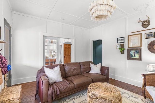 living area featuring a chandelier, coffered ceiling, baseboards, and wood finished floors