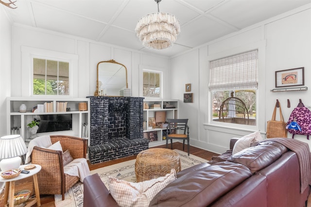 living area with a brick fireplace, a chandelier, wood finished floors, a decorative wall, and coffered ceiling