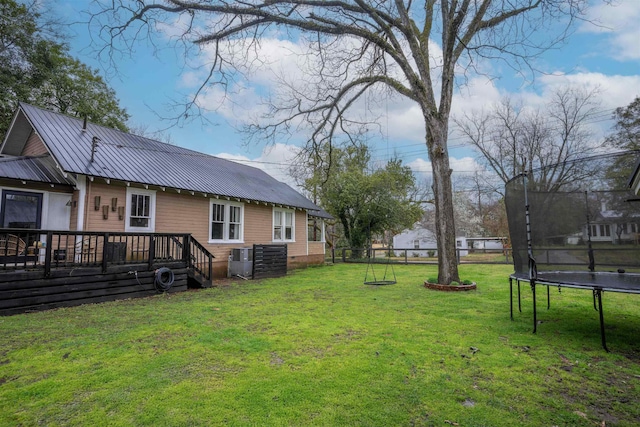 view of yard featuring a wooden deck, a trampoline, central AC, and fence