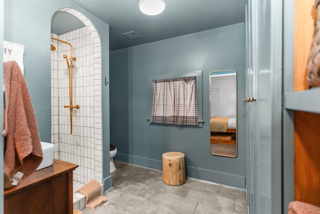 bathroom with a tile shower, visible vents, toilet, and baseboards