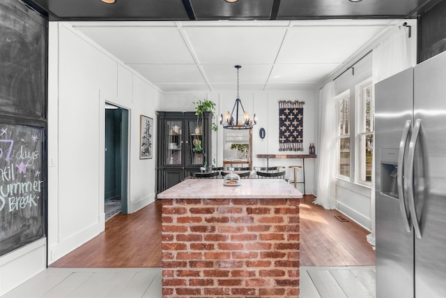 kitchen featuring stainless steel fridge, an inviting chandelier, wood finished floors, and a center island