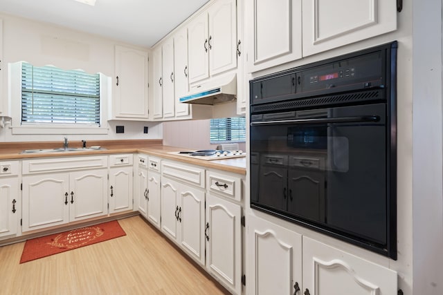 kitchen featuring a sink, white stovetop, black oven, white cabinetry, and under cabinet range hood