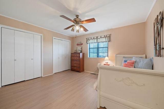 bedroom featuring crown molding, multiple closets, ceiling fan, and light wood-type flooring