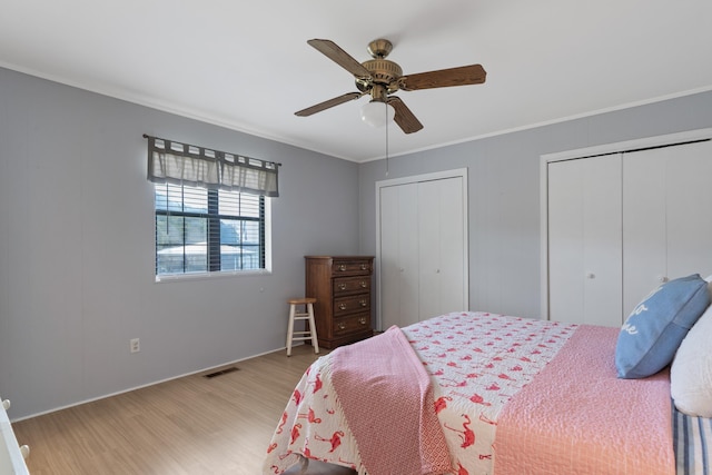 bedroom featuring visible vents, baseboards, multiple closets, ornamental molding, and light wood-style flooring