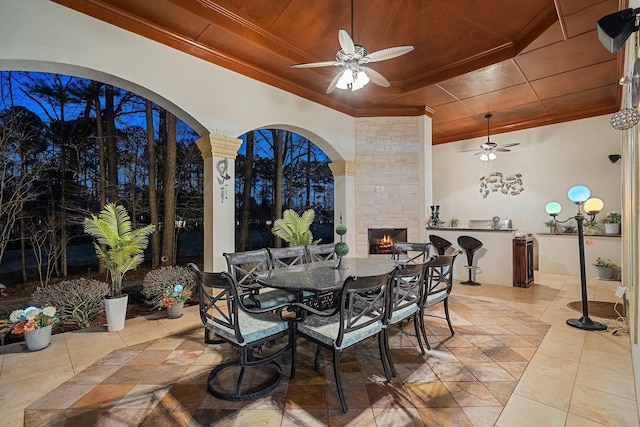 tiled dining room with an outdoor stone fireplace, wooden ceiling, crown molding, and a tray ceiling