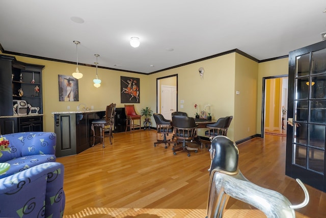 living room with light wood-type flooring, indoor wet bar, baseboards, and ornamental molding