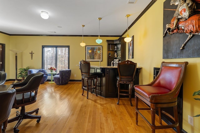 interior space with crown molding, baseboards, decorative light fixtures, wood finished floors, and a bar