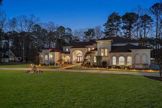 mediterranean / spanish-style home featuring french doors, curved driveway, a front lawn, and stucco siding