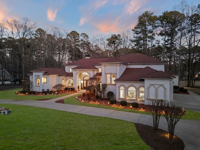 mediterranean / spanish home featuring a yard, curved driveway, a chimney, and stucco siding