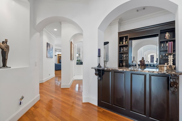 bar featuring visible vents, ornamental molding, baseboards, light wood finished floors, and wet bar